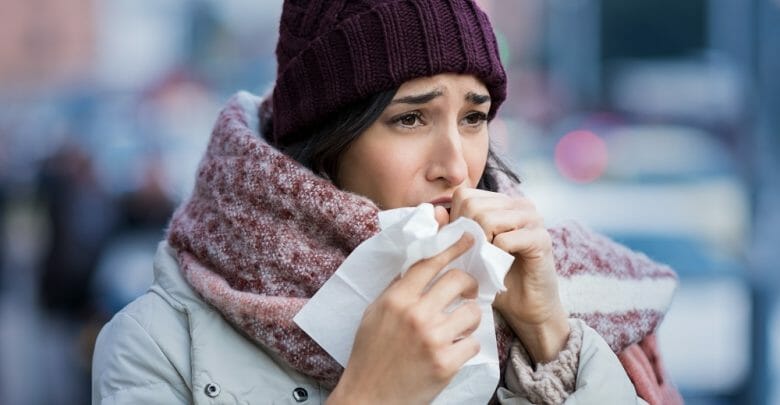 Young woman coughing during winter on street. Girl with cold wearing knitted cap and scarf feeling unwell. Woman feeling sick during for winter and city pollution. Girl with sore throat.